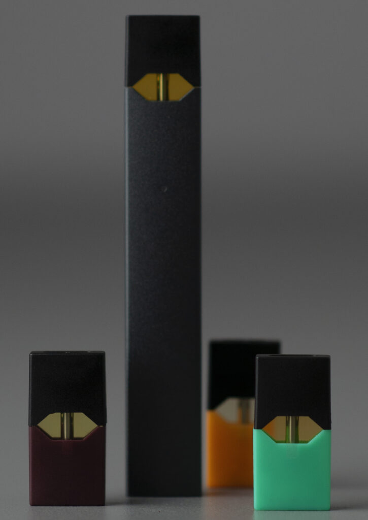 Black vape device standing upright with colored pods beside it